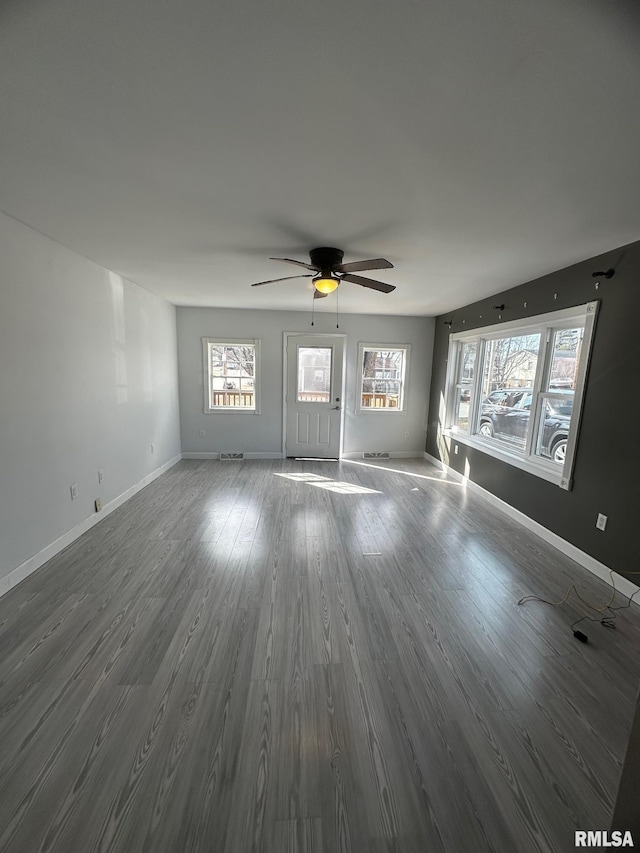 unfurnished living room featuring a ceiling fan, baseboards, and dark wood-style flooring