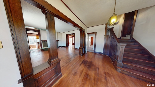 entrance foyer featuring a textured ceiling, wood finished floors, stairway, decorative columns, and baseboards