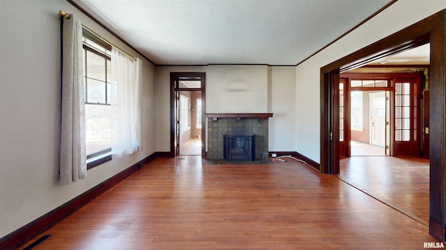 unfurnished living room featuring a textured ceiling, wood finished floors, baseboards, and a tile fireplace