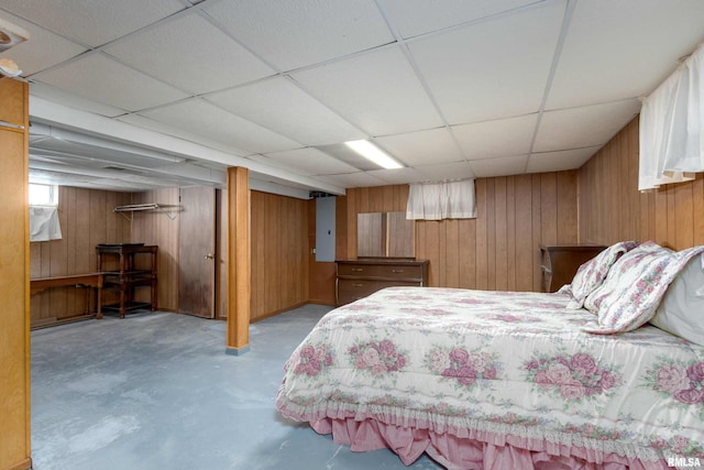 bedroom with wooden walls, a drop ceiling, and finished concrete floors