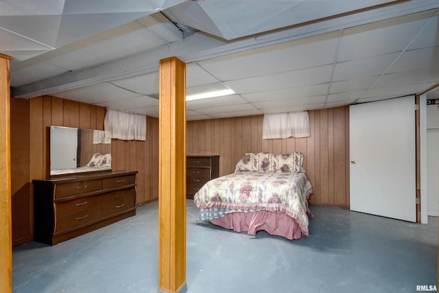 bedroom featuring a drop ceiling, concrete flooring, and wood walls