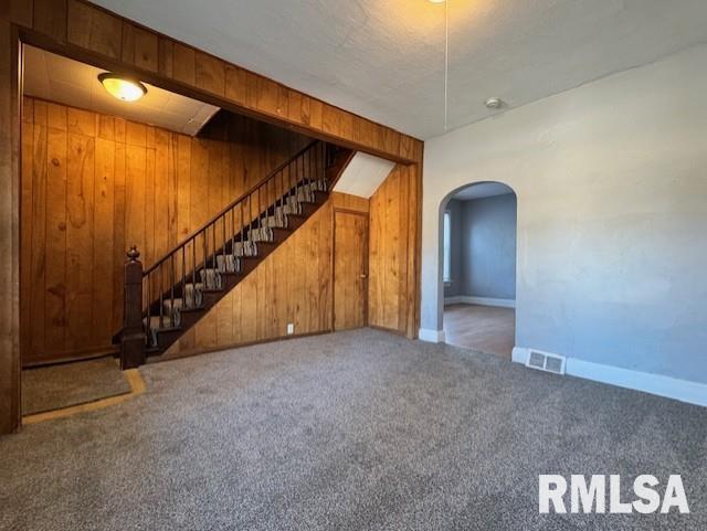 unfurnished living room featuring visible vents, stairway, arched walkways, wooden walls, and carpet