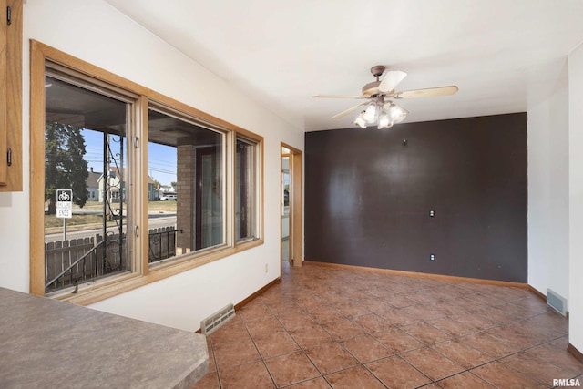 tiled spare room with visible vents, ceiling fan, and baseboards