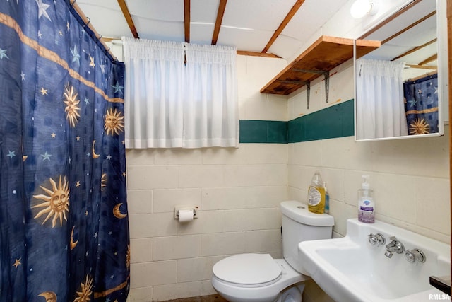 full bath with a sink, toilet, a shower with shower curtain, and concrete block wall