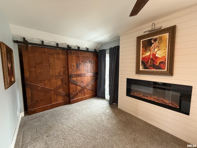 unfurnished living room featuring wooden walls, a barn door, lofted ceiling, carpet flooring, and a glass covered fireplace