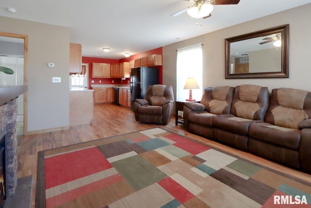 living area with a stone fireplace, a ceiling fan, and light wood-type flooring