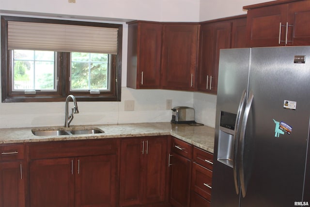 kitchen with a sink, reddish brown cabinets, stainless steel refrigerator with ice dispenser, and light stone countertops