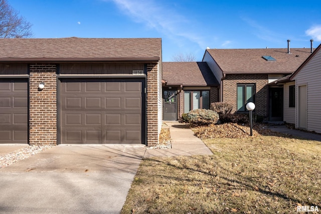 single story home with concrete driveway, an attached garage, brick siding, and roof with shingles