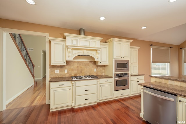 kitchen with stainless steel appliances, tasteful backsplash, wood finished floors, and dark stone counters