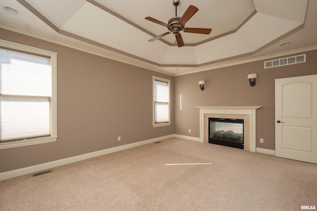 unfurnished living room with a tray ceiling, visible vents, a glass covered fireplace, and ornamental molding