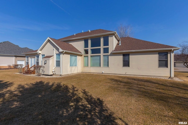 back of property with a yard, roof with shingles, and entry steps