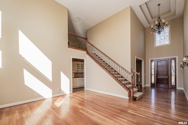 foyer entrance with stairway, wood finished floors, baseboards, a towering ceiling, and a notable chandelier