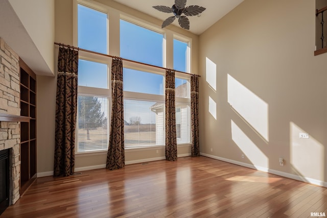 unfurnished living room featuring a stone fireplace, hardwood / wood-style floors, and a towering ceiling