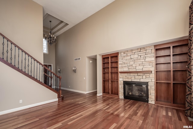 unfurnished living room featuring visible vents, wood finished floors, stairway, an inviting chandelier, and baseboards