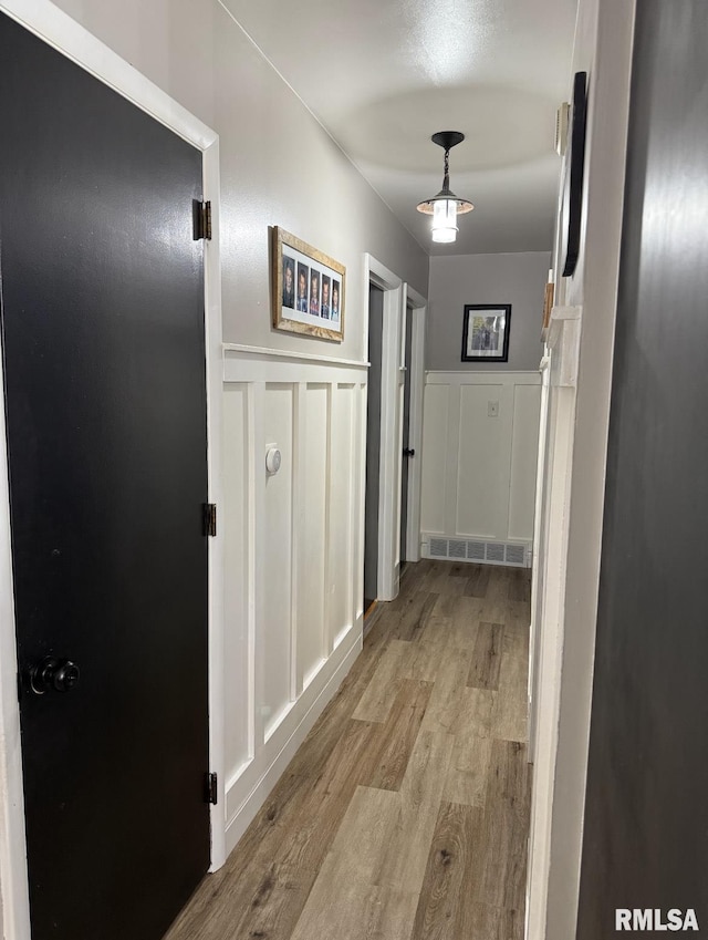 hall with visible vents, light wood-style flooring, wainscoting, and a decorative wall