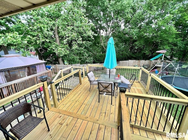 wooden deck featuring a playground, outdoor dining area, and a fenced backyard