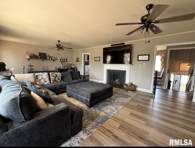 living area featuring baseboards, a ceiling fan, wood finished floors, and a fireplace