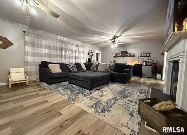 living area featuring baseboards, wood finished floors, ceiling fan, and a fireplace