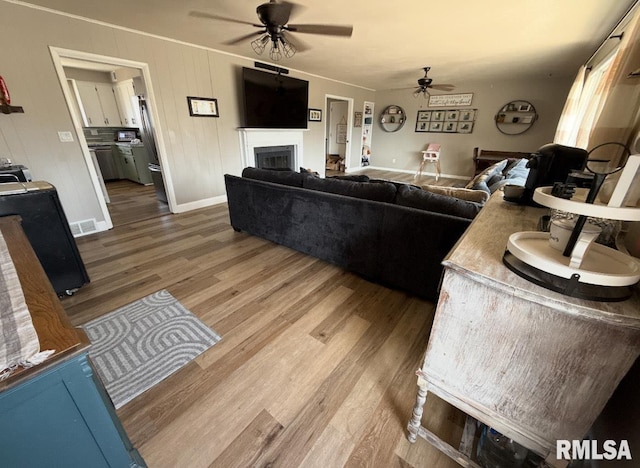 living area with visible vents, baseboards, ceiling fan, a fireplace, and wood finished floors