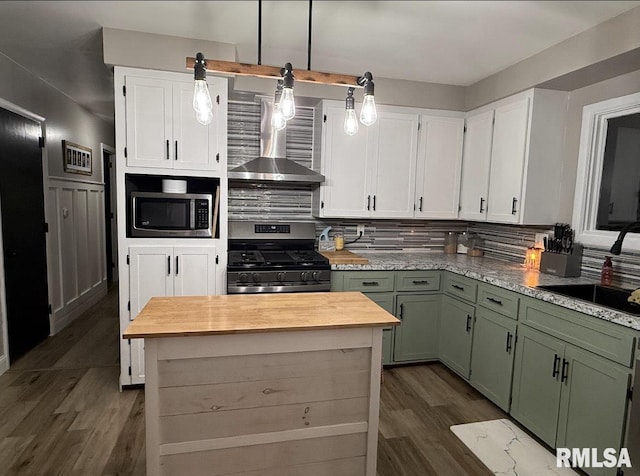 kitchen featuring green cabinetry, a sink, stainless steel appliances, wood counters, and wall chimney range hood