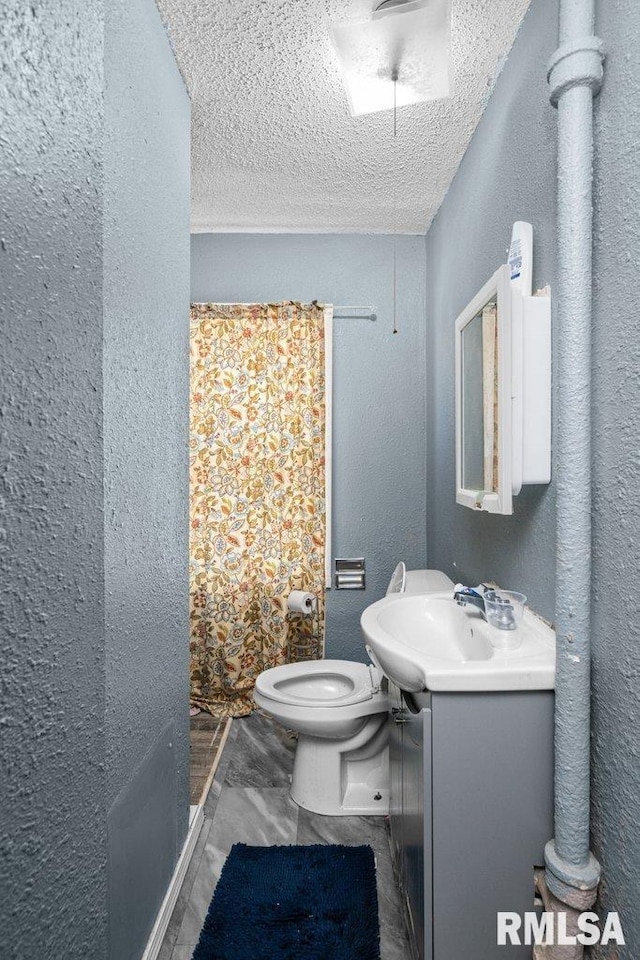 bathroom featuring vanity, toilet, a textured wall, and a textured ceiling