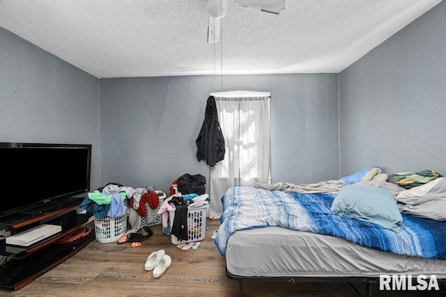 bedroom featuring a textured ceiling, wood finished floors, a ceiling fan, and a textured wall