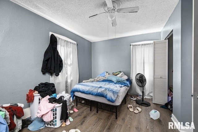 bedroom with ceiling fan, a textured ceiling, a textured wall, and wood finished floors