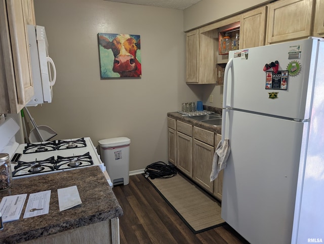 kitchen featuring dark countertops, dark wood-style floors, white appliances, and light brown cabinetry