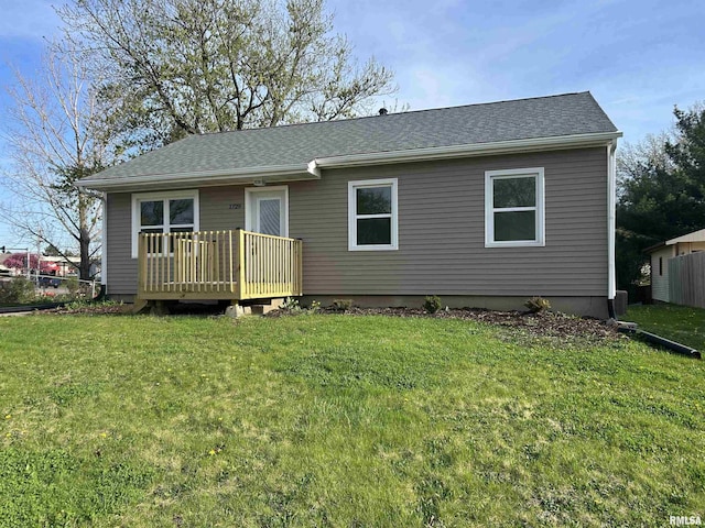 view of front of house featuring fence, a wooden deck, a front lawn, and roof with shingles