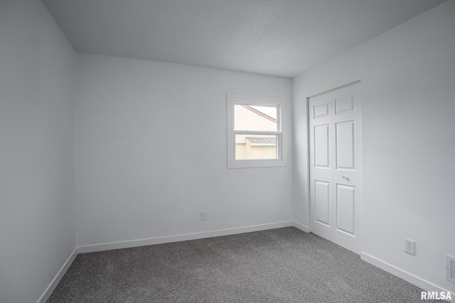 empty room with dark carpet, a textured ceiling, and baseboards