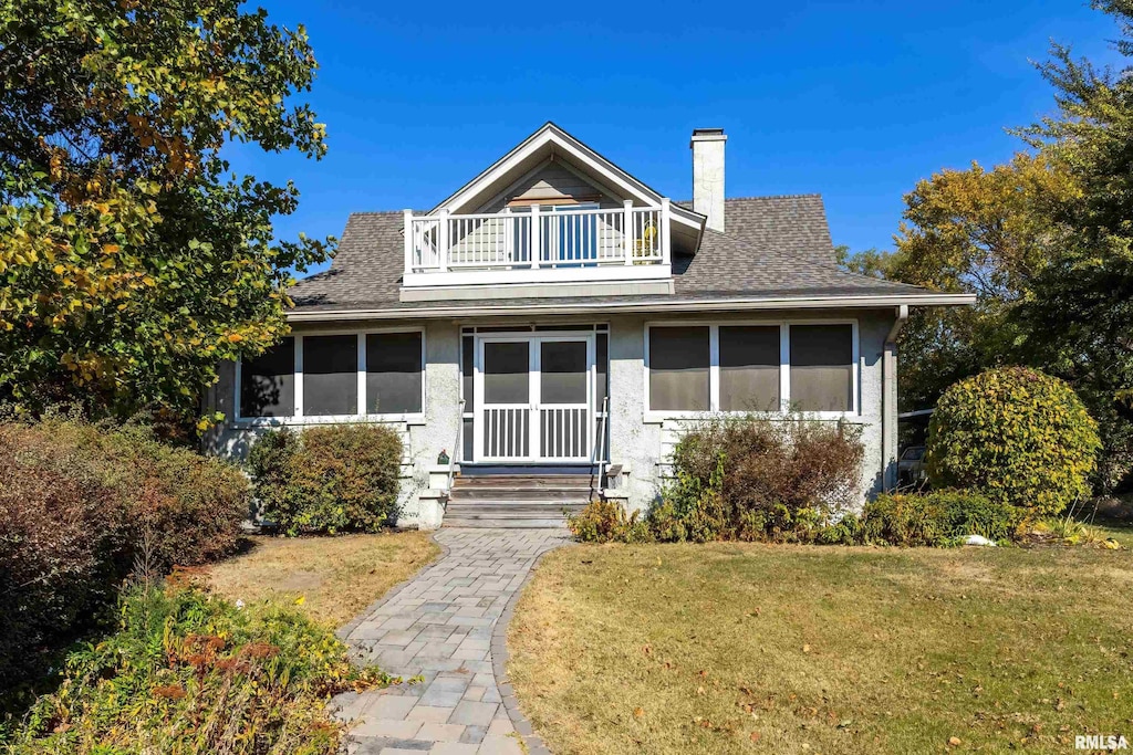 bungalow-style home featuring a front yard, a chimney, a shingled roof, and a balcony