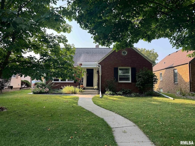 view of front of house with brick siding, a chimney, a front lawn, and roof with shingles