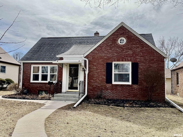 bungalow-style house featuring brick siding, a chimney, and roof with shingles