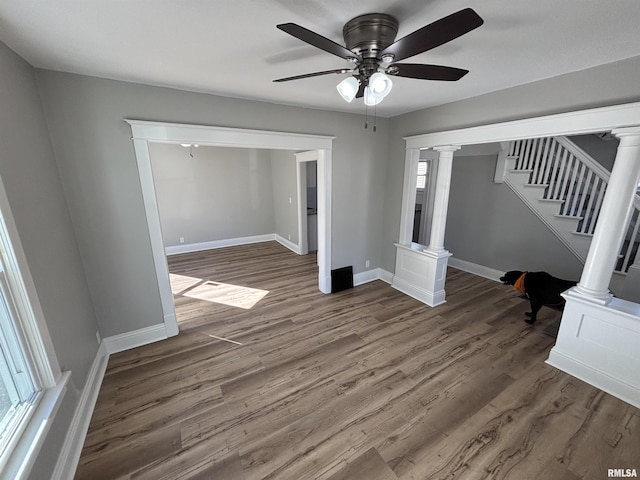 empty room with decorative columns, baseboards, wood finished floors, and stairway