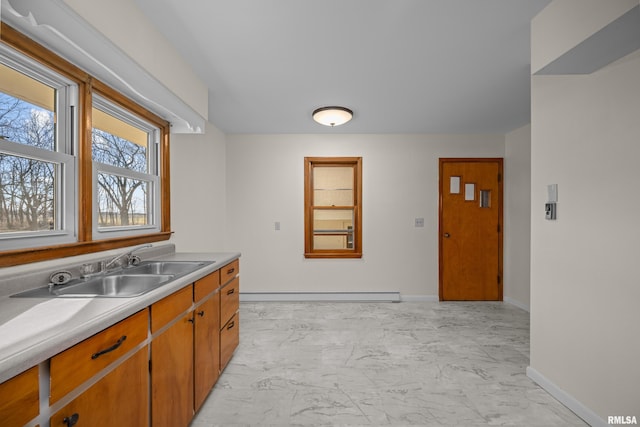 kitchen with baseboards, light countertops, baseboard heating, marble finish floor, and a sink