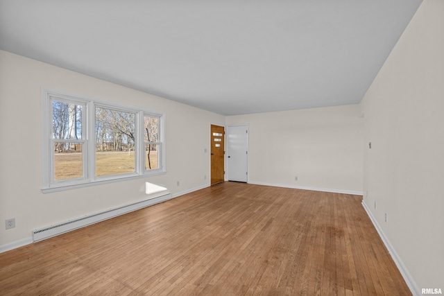 spare room featuring a baseboard radiator, baseboards, and hardwood / wood-style flooring