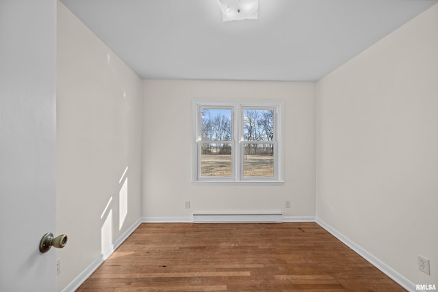 empty room featuring a baseboard heating unit, baseboards, and wood finished floors