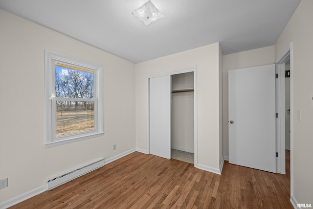 unfurnished bedroom featuring a closet, wood finished floors, baseboards, and a baseboard radiator