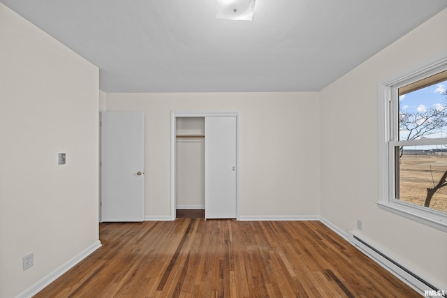 unfurnished bedroom featuring baseboards, wood-type flooring, baseboard heating, and a closet