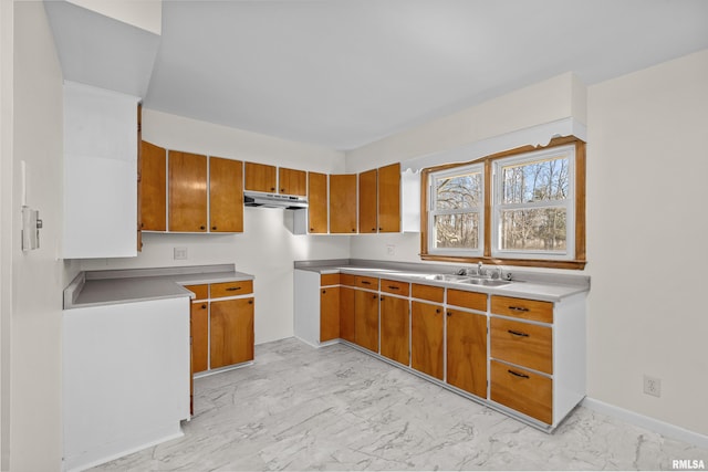 kitchen featuring under cabinet range hood, light countertops, brown cabinets, marble finish floor, and a sink