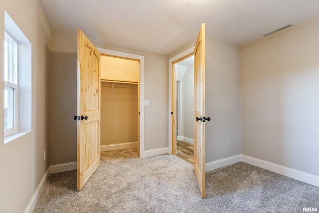 unfurnished bedroom with light carpet, visible vents, a walk in closet, and baseboards