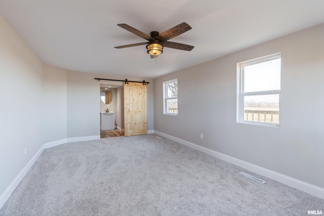 unfurnished bedroom featuring visible vents, baseboards, a barn door, and carpet floors