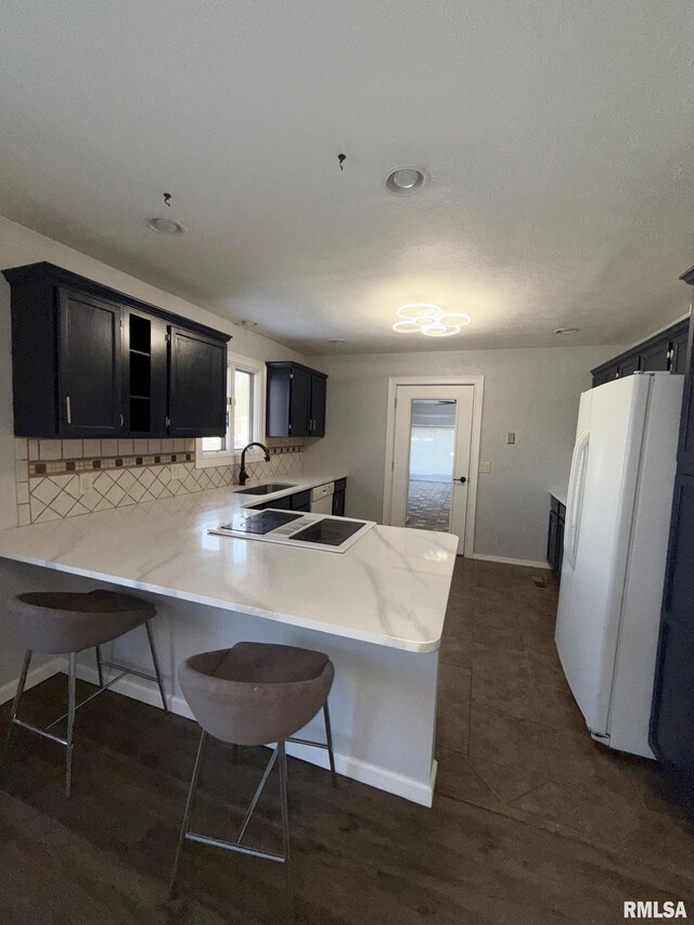 kitchen with decorative backsplash, a kitchen bar, dark cabinets, and freestanding refrigerator