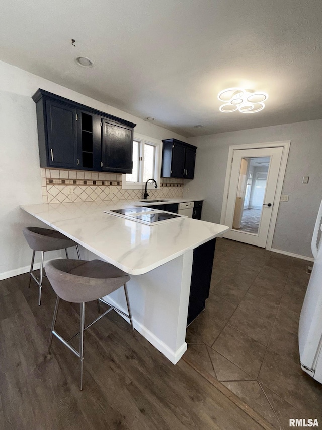 kitchen with a kitchen bar, backsplash, a peninsula, and dark cabinets