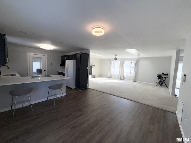 kitchen featuring a breakfast bar area, dark wood-style floors, a peninsula, a sink, and white fridge with ice dispenser