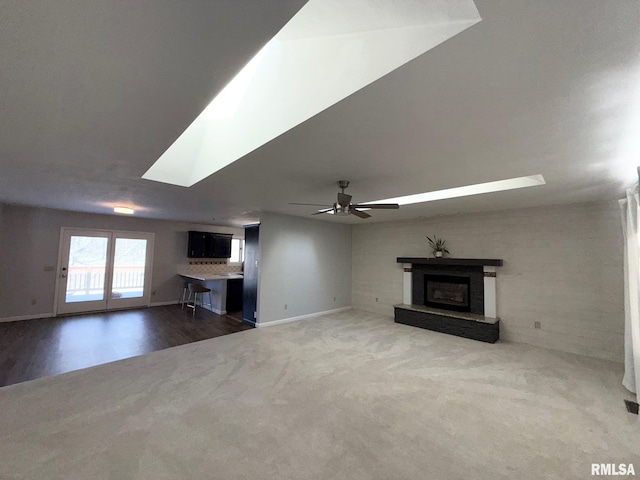 unfurnished living room with a fireplace with raised hearth, baseboards, ceiling fan, carpet flooring, and a skylight