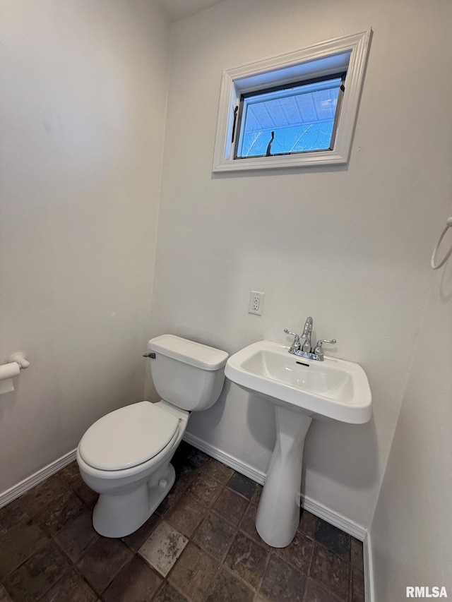 bathroom featuring a sink, stone finish flooring, baseboards, and toilet