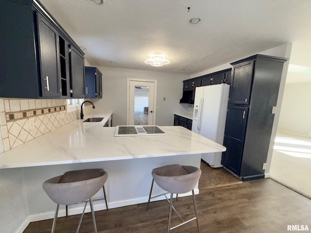 kitchen with a breakfast bar, a sink, white refrigerator with ice dispenser, a peninsula, and stovetop with downdraft