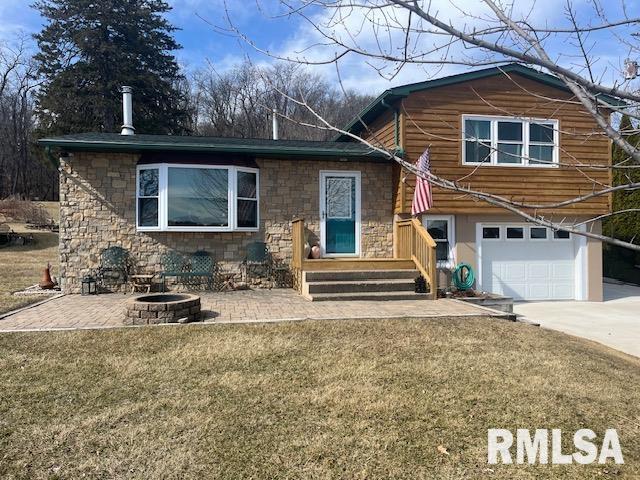 view of front facade with stone siding, a fire pit, an attached garage, and a front yard