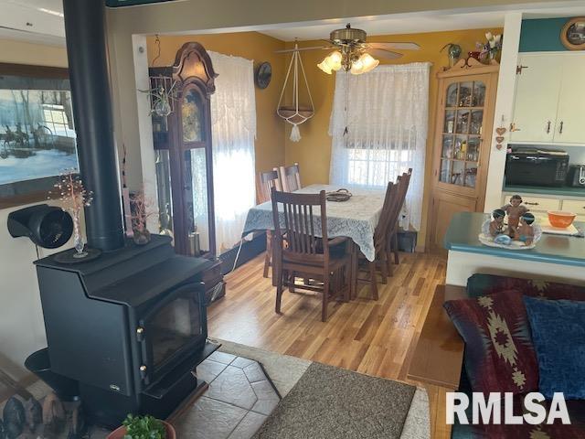 dining area featuring a wealth of natural light, light wood-type flooring, a ceiling fan, and a wood stove